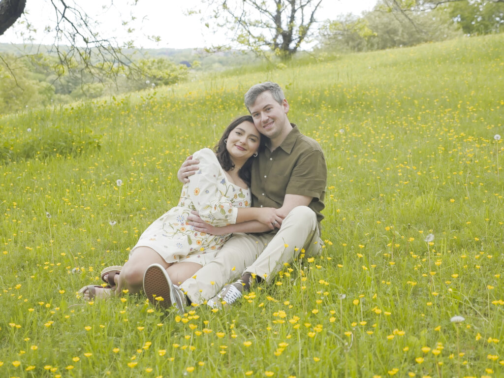 Engaged couple sitting together in a field of buttercups